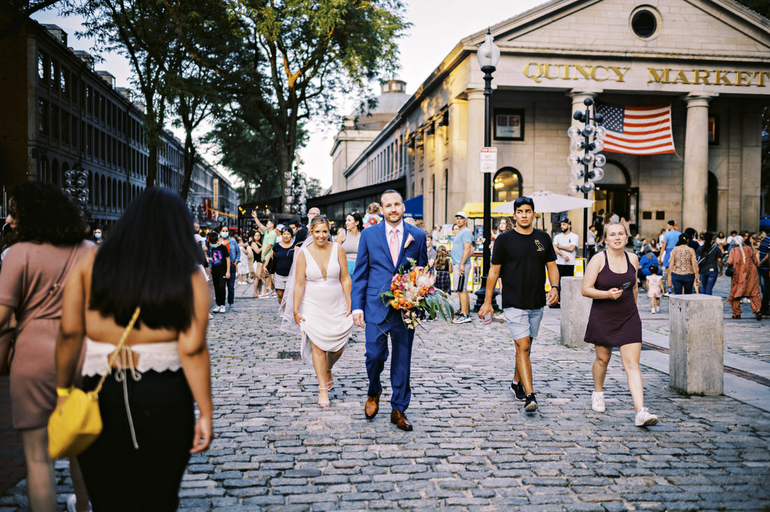 Groom holding flowers walking with the bride through Quincy Market