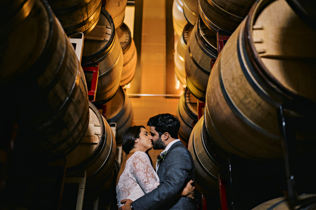 Bride and groom kissing among the barrels at Newport Vineyard