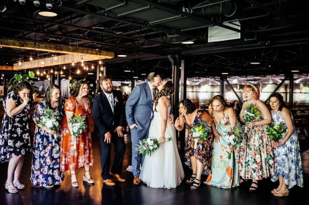 Bride kissing groom while friends make a face