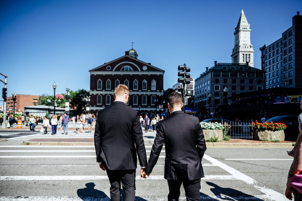 Grooms holding hands walking to Quincy Market on wedding day 