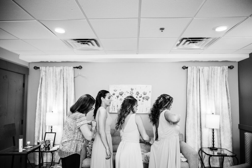 Bridesmaids all zipping each others dresses, candid wedding photos 