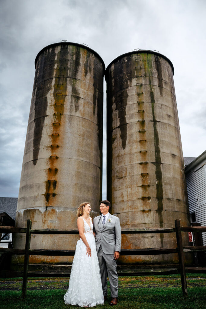 Bride and groom laughing with each other outside in front of some silos